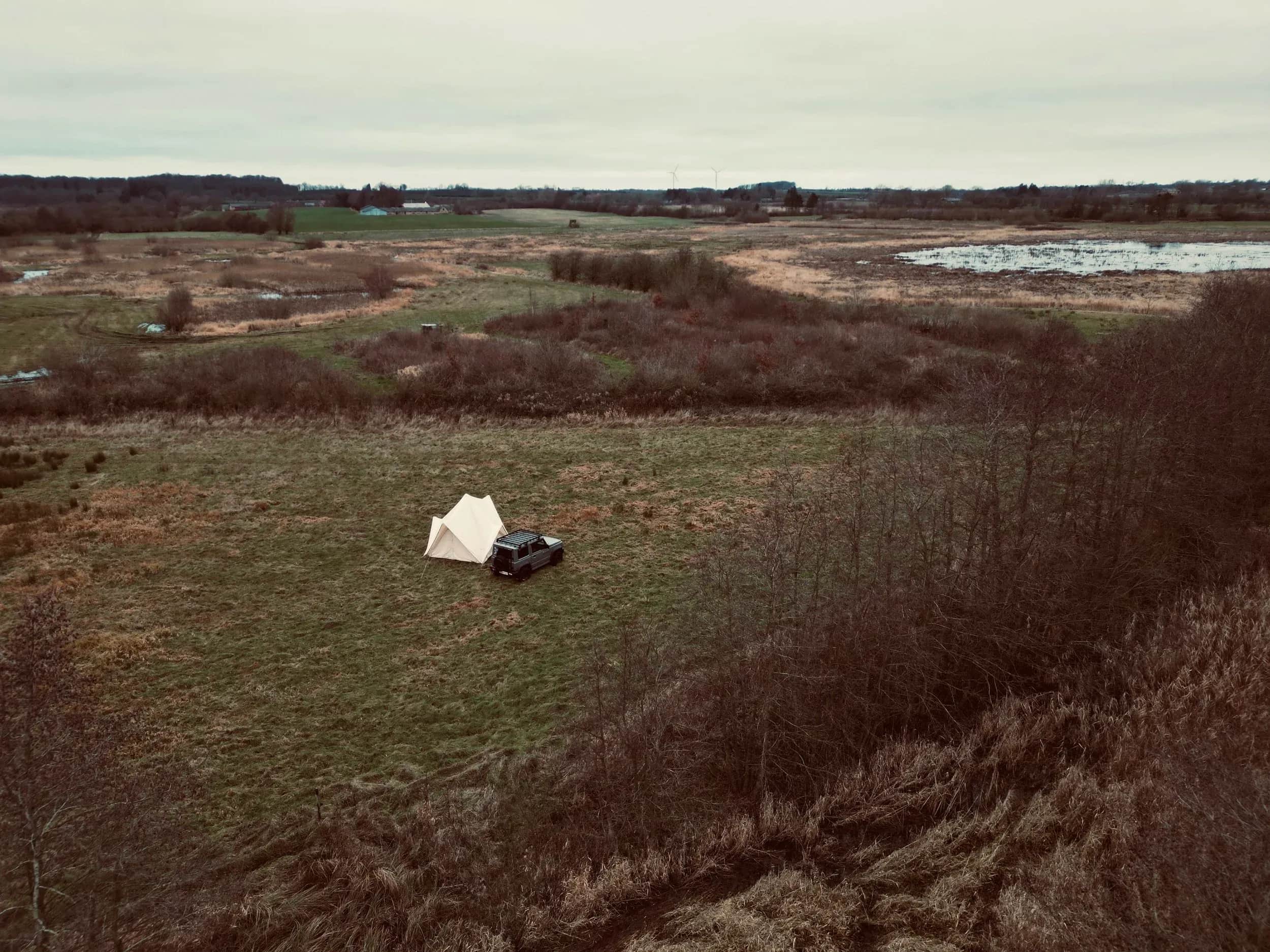 Beige telt og en bil på en skrænt over et fladt landskab.