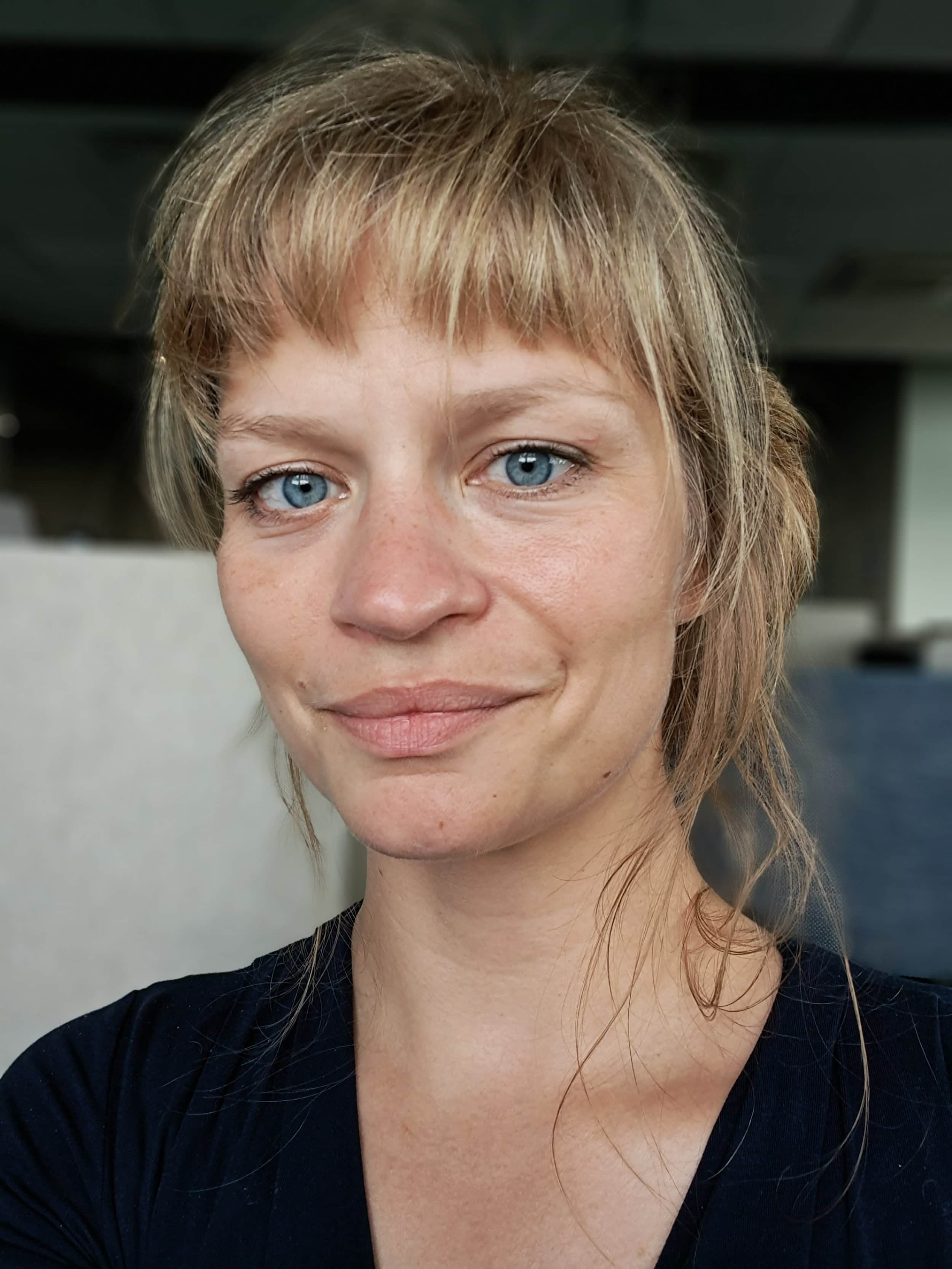 Portræt af en kvinde med lyst pagehår og mørk bluse.