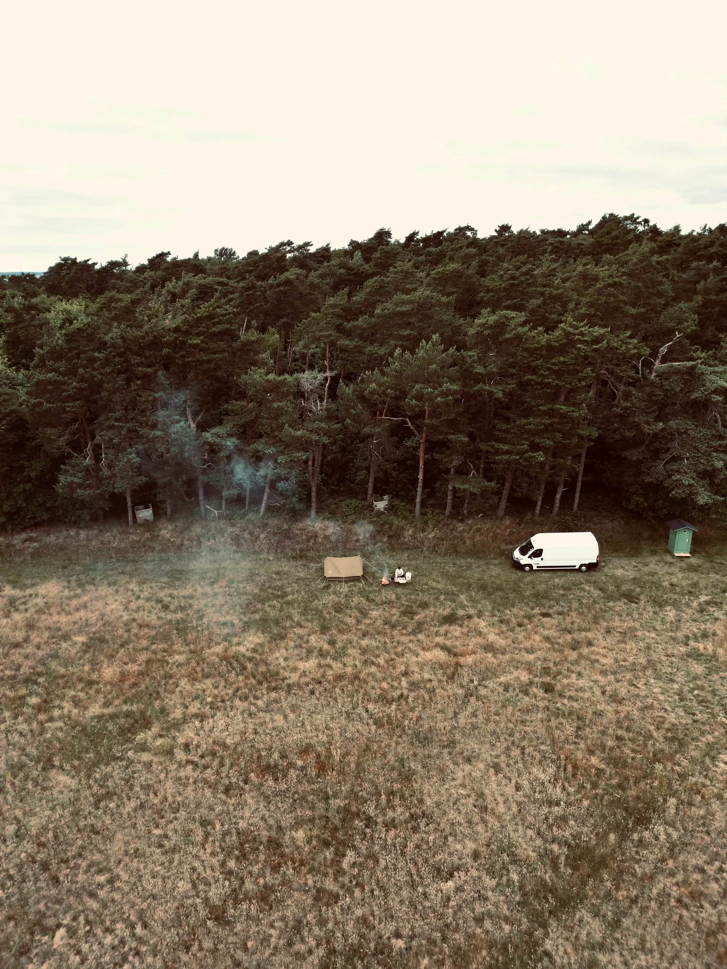 Luftfoto af en hvid varevogn på en lysning foran fyrreskov.
