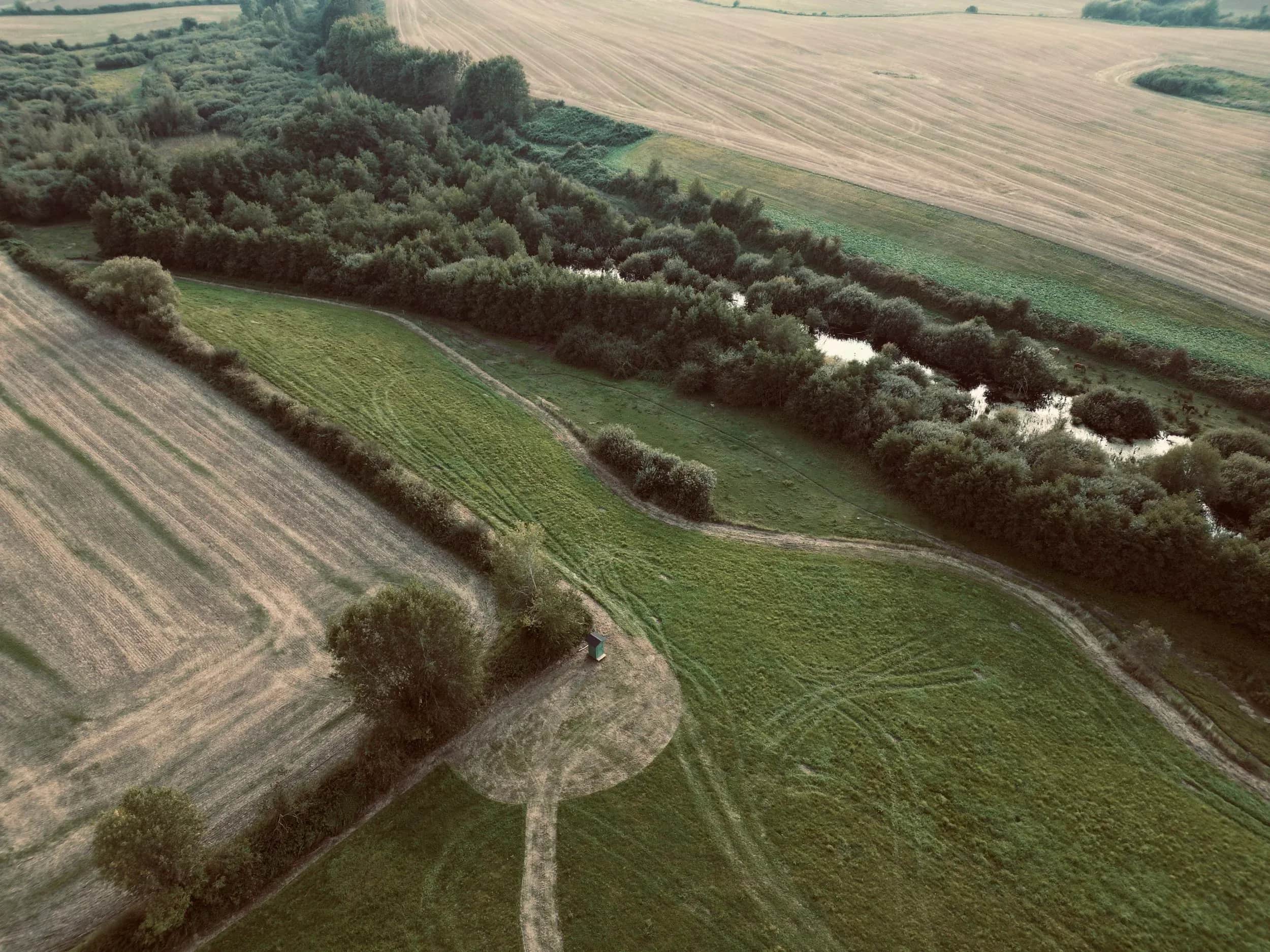 Luftfoto af marker, hegn og et vandløb.