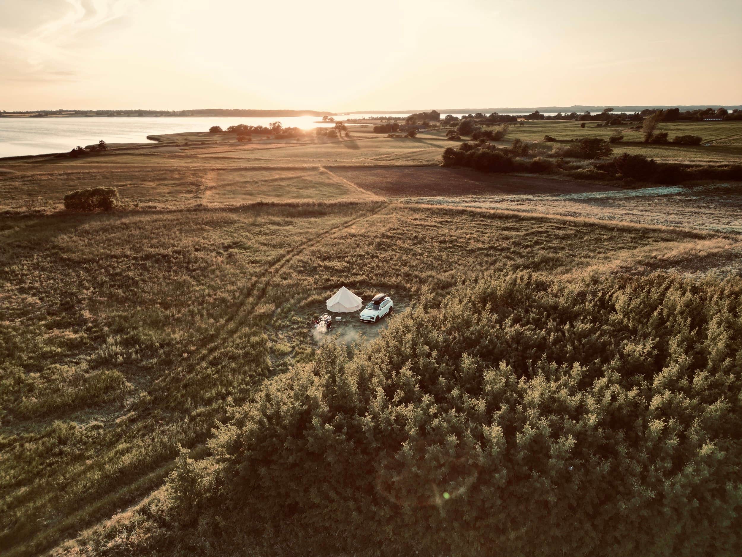 Luftfoto af et telt og en bil på en skrænt ned mod vand i solnedgang.